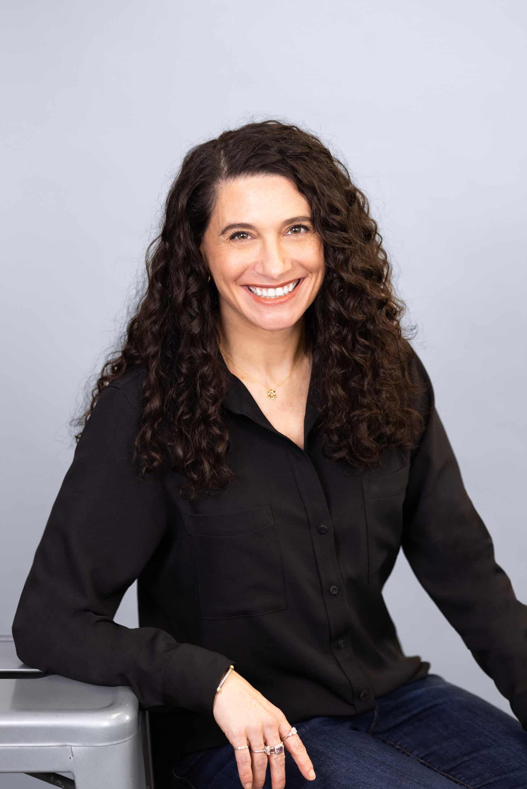 smiling woman with long wavy dark hair wearing a black long sleeved shirt