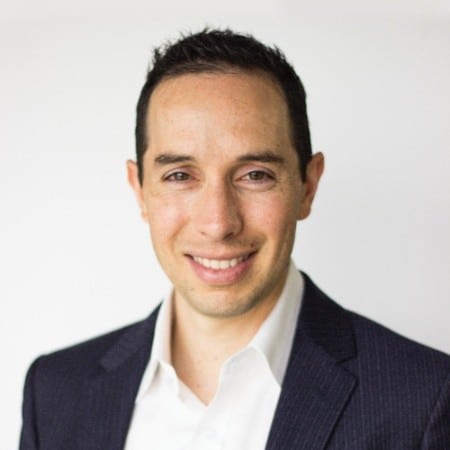 smiling man with close-cropped dark hair in dark jacket and white dress shirt open at the collar