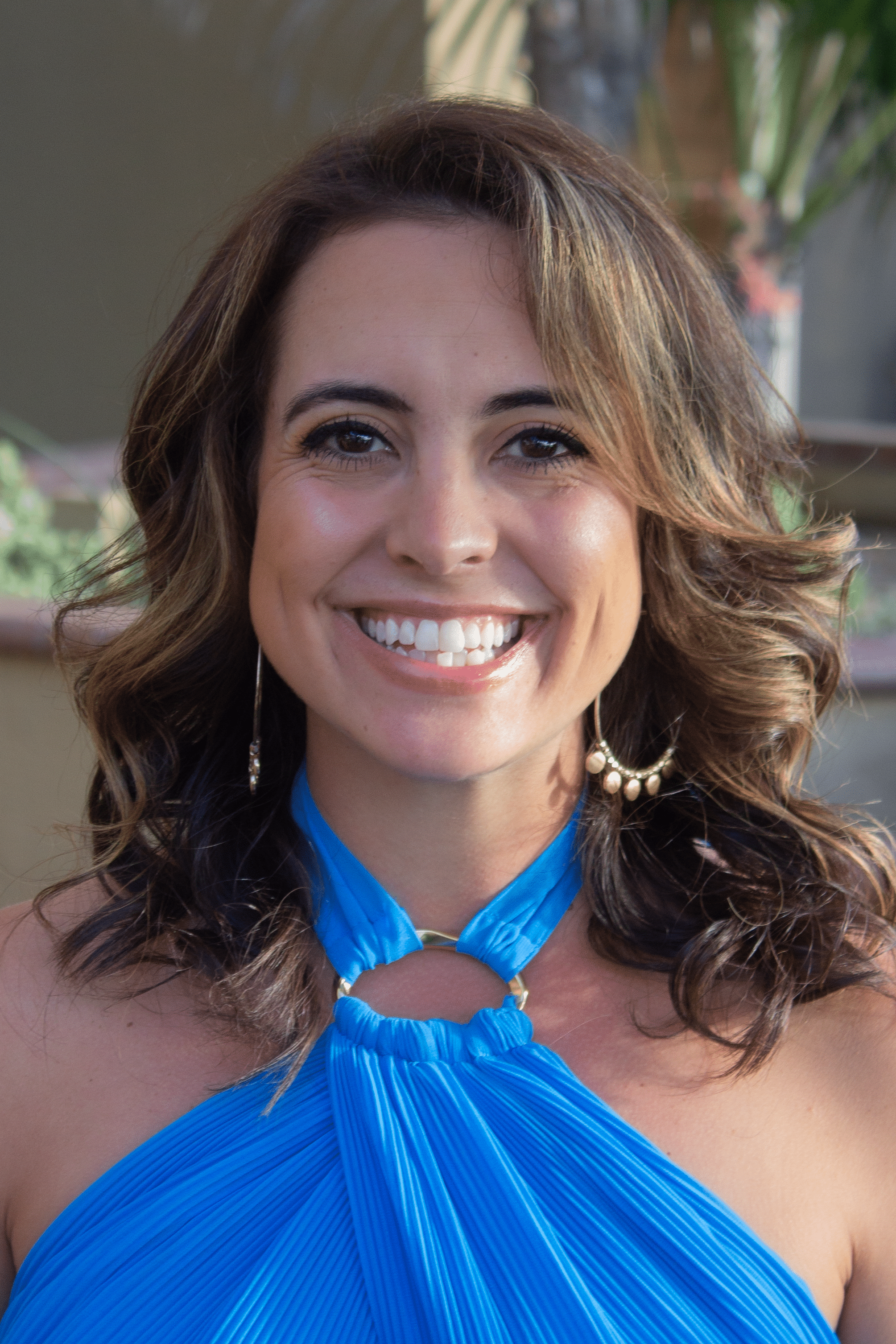 Lee Ann Mazzarisi portrait, smiling woman with long wavy brown hair wearing bright blue halter blouse